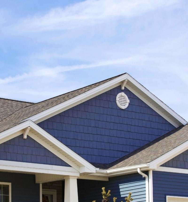 Blue sided contemporary home showing soffit, gutters, roofing, brickwork, and blue sky in the background. Blue sided contemporary home showing soffit, gutters, roofing, brickwork, and blue sky in the background.